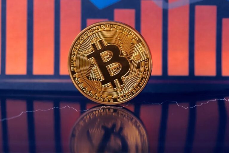 Physische Bitcoin-Münze vor einem rot absteigenden Kurs-Chart und Aktiendiagramm