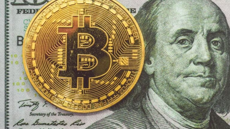 Ein abwärts gerichteter roter Kurs-Chart im Hintergrund einer physischen Bitcoin-Münze