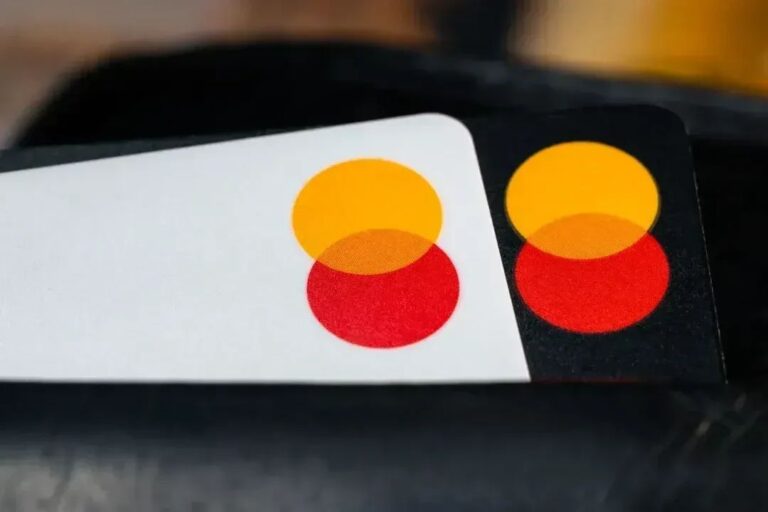 Eine Kreditkarte von Mastercard neben digitalen Münzen von Ripple und Solana vor einem modernen Finanz-Chart.