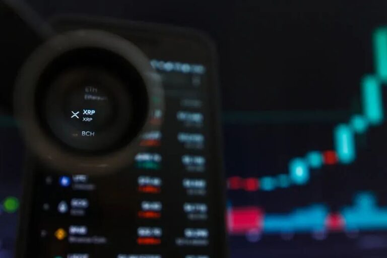 Eine physische XRP-Münze vor einem unscharfen Hintergrund mit einem digitalen Kurs-Chart.