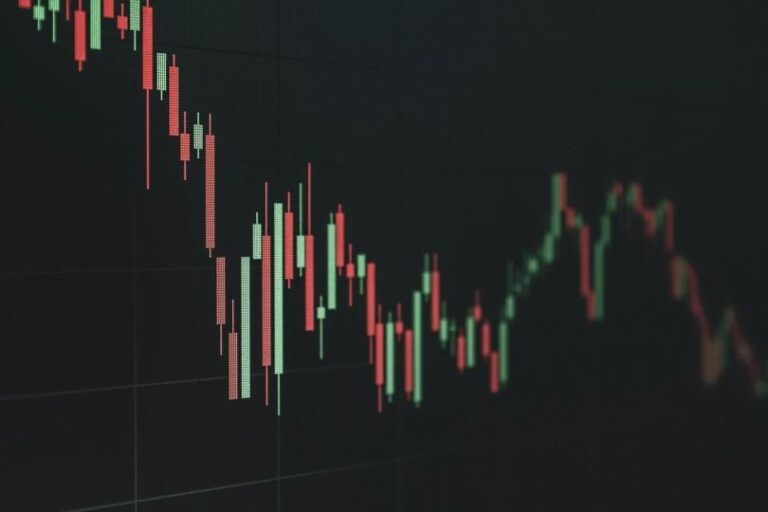 Physische Bitcoin-Münze vor einem volatilen Kurs-Chart im Hintergrund