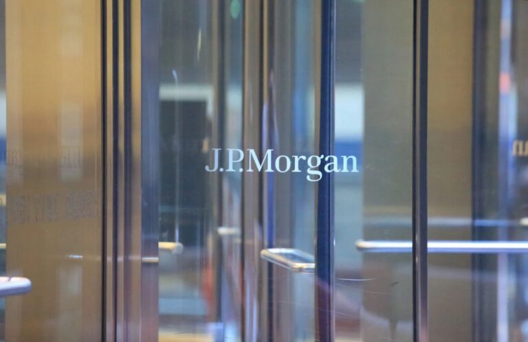 JPMorgan-Gebäude im Hintergrund mit einer physischen Bitcoin-Münze im Vordergrund auf einem abstrakten Kurs-Chart