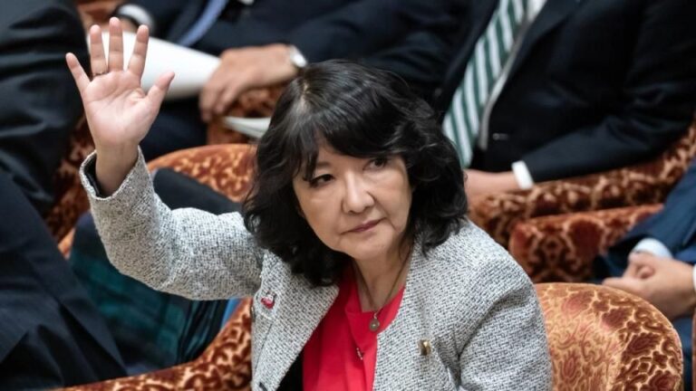 Die japanische Finanzministerin Satsuki Katayama vor einem Kurs-Chart für Bitcoin und Gold.