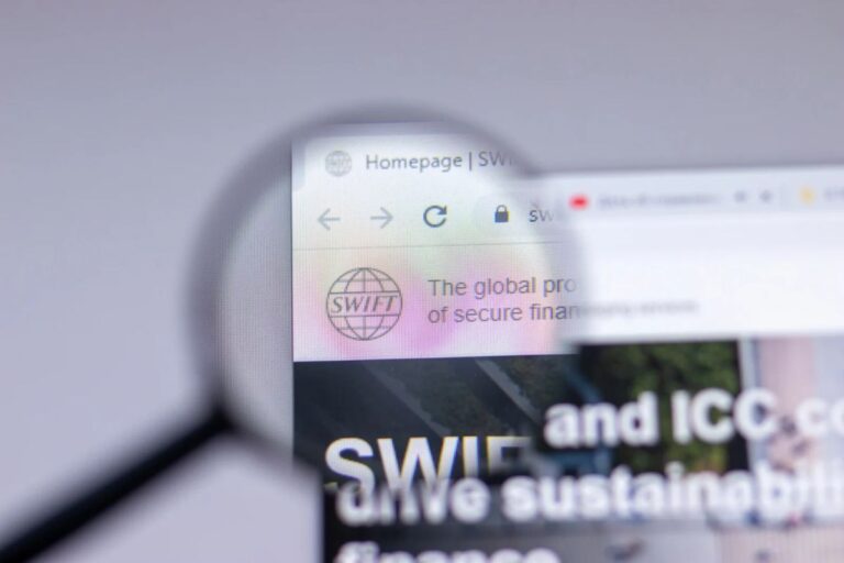 Silberne XRP-Münze neben dem blauen SWIFT-Logo vor einem abstrakten digitalen Hintergrund.