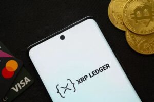 Ein glänzender Goldbarren liegt neben einer XRP-Münze auf einem digitalen Kurs-Chart