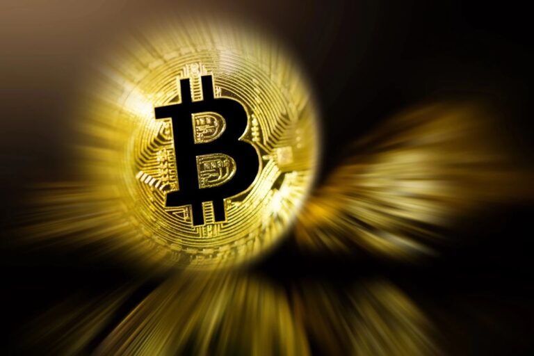 Bitcoin-Münze auf einem Smartphone-Display mit einem im Hintergrund abfallenden Börsen-Chart