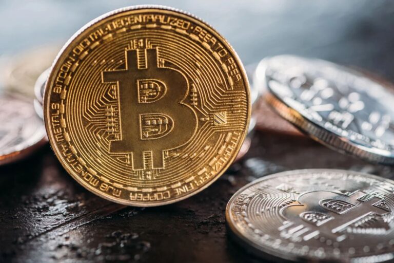Roter fallender Kurs-Chart auf einem Bildschirm hinter einer physischen Bitcoin-Münze