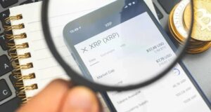 Ein abwärtsgerichteter Kurs-Chart mit roten Kerzen hinter einer physischen Ripple-Münze